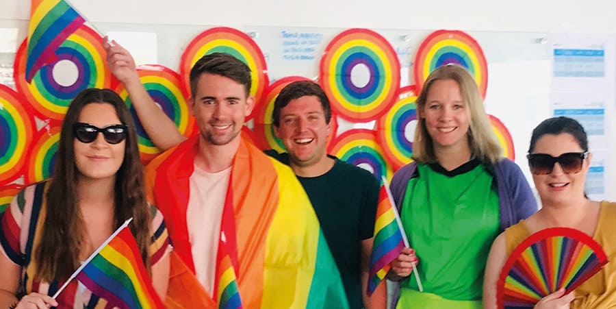 A group of young people dressed for Pride parade, wearing rainbow clothes and smiling.